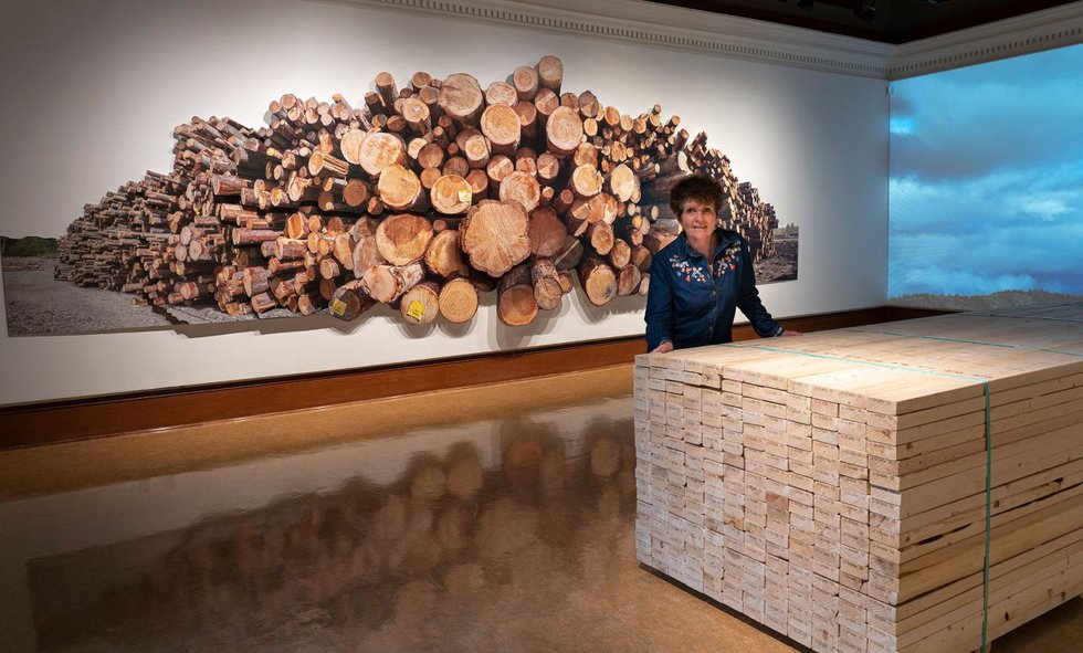 Fern Helfand poses in front of "Log Pile," part of her exhibition, "Timber, Lumber, Wood, Home," at the Grand Forks Art Gallery in British Columbia. (courtesy of artist)
